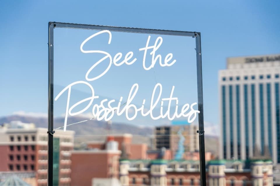 Neon sign reading See the Possibilities in front of a city skyline